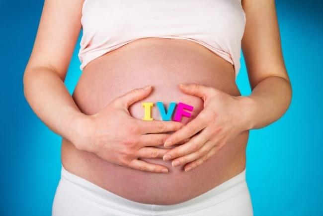 אישה בהריון שעל הבטן שלה מונחות האותית IVF,הורמון HMG